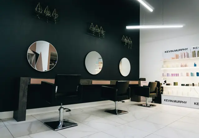 Svarte frisørstoler foran runde speil på en mørk vegg